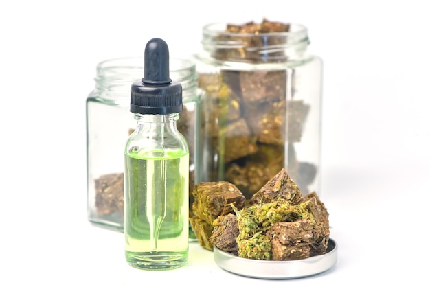 Glass bottle of cannabis oil and a jar of dried cannabis on a white background CBD Hemp oilhemp oil Medical marijuana products including cannabis leaf cbd and hash oil alternative medicine