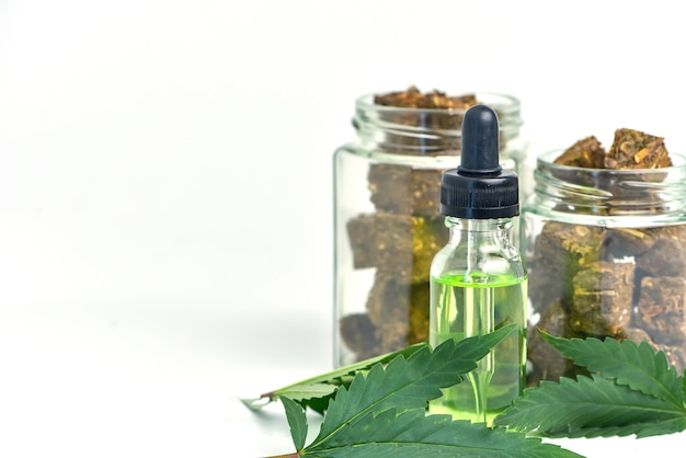 Glass bottle of cannabis oil and a jar of dried cannabis on a white background CBD Hemp oilhemp oil Medical marijuana products including cannabis leaf cbd and hash oil alternative medicine