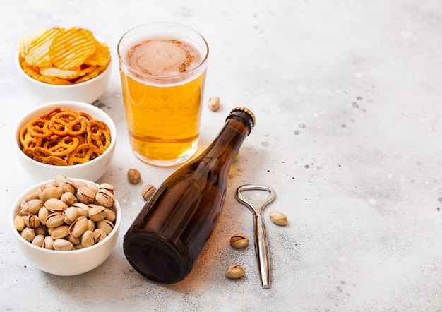 Glass and bottle of craft lager beer with snack and opener on stone kitchen table