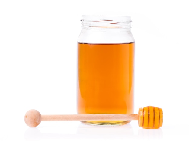 Glass bottle full of honey and wooden stick on a white background.