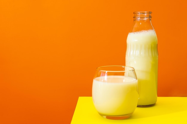 Glass bottle and large glass with milk on a yellow table with orange background