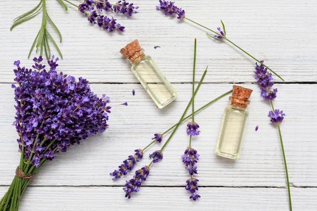 Glass bottle of lavender essential oil with fresh lavender flowers and on white wooden rustic table aromatherapy spa massage concept lavender oil