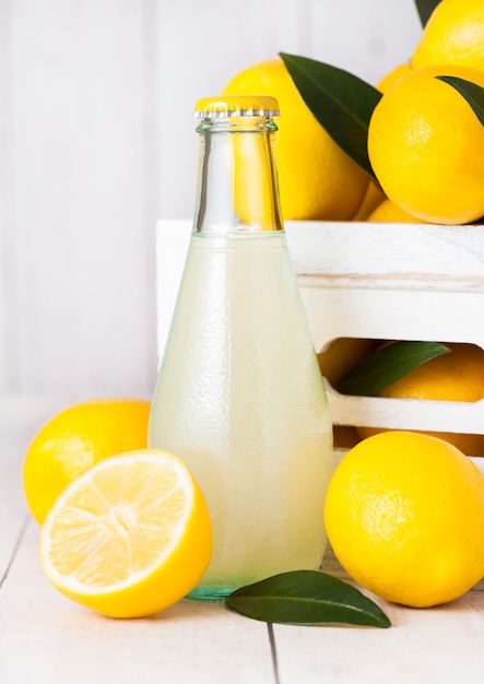 Glass bottle of organic fresh lemon juice with raw lemons in white wooden box