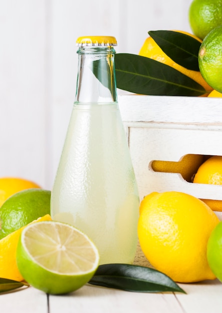 Glass bottle of organic fresh lemon and lime  juice with raw lemons and limes in white wooden box