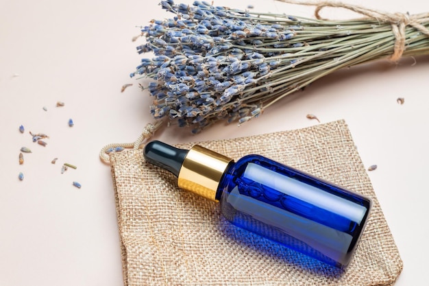 Glass bottle with cosmetic oil or serum and lavender flowers around it on a beige background Concept of lavender fragrance skin care Mockup