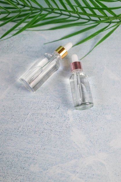 glass bottle with a cosmetic product with a pipette for skin care on the background of a palm leaf