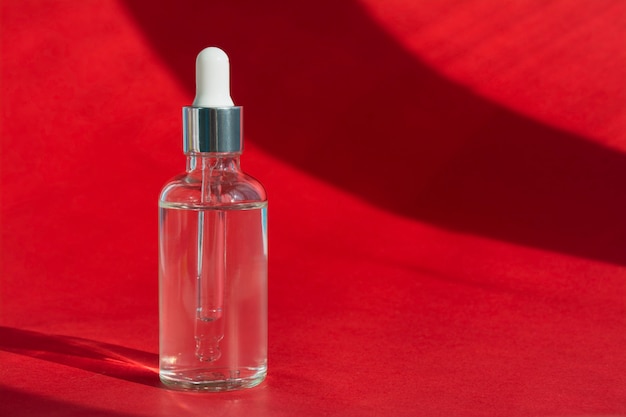 Glass bottle with a dropper on a red background, hard light. Liquid face serum with collagen. Skin care. Copy space.