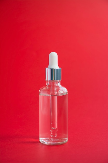 Glass bottle with a dropper on a red background, hard light. Liquid face serum with collagen. Skin care. Copy space.