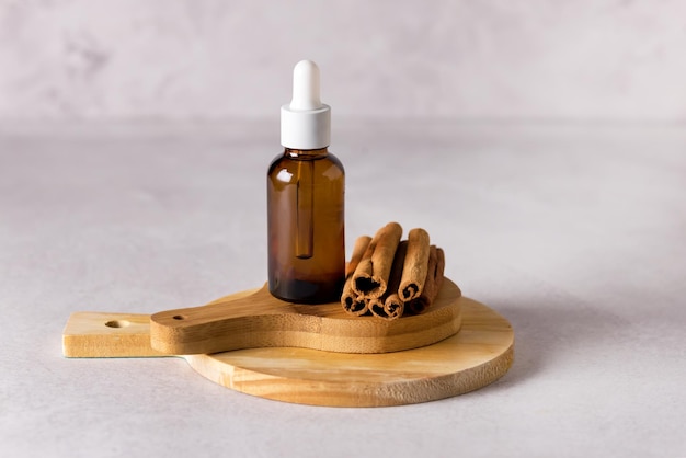 Glass Bottle with Essential Cinnamon Oil and Sticks on Wooden Board Gray Background