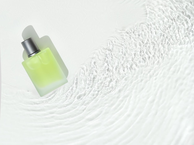 Glass bottle with green product in water. White transparent water texture. Top view on surface with waves and ripples. Flat lay, copy space.