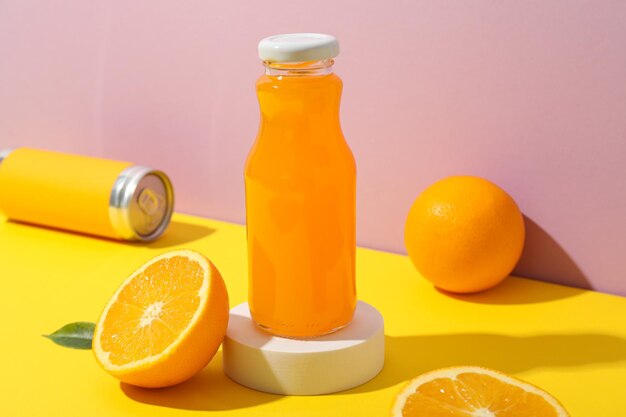 Glass bottle with juice oranges and tin can on pink background