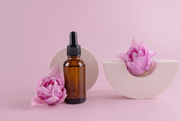 Glass bottle with natural cosmetics serum oil for face and body skin care on the background of concrete geometric shapes and flowers