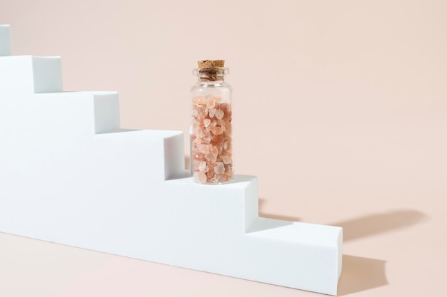 A glass bottle with pink salt for spa procedures standing on a white stairs