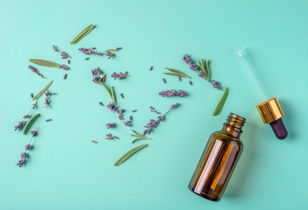 Glass bottle with a pipette and leaves and flowers on a bluegreen background Concept of lavender fragrance