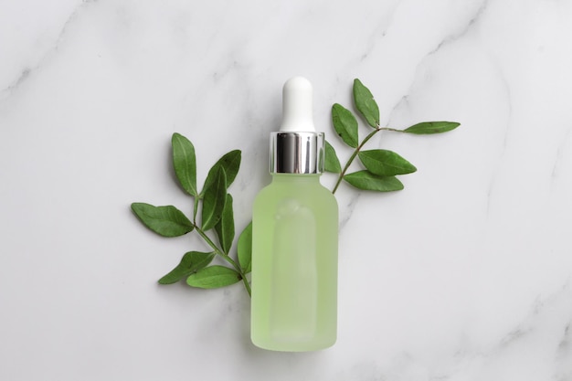 Glass bottle with serum and leaves on marble background