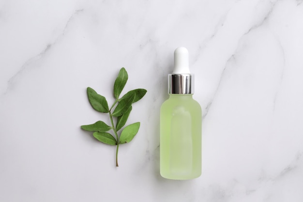 Glass bottle with serum and leaves on marble background