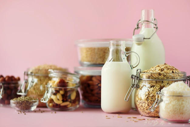 Glass bottles of vegan plant milk and almonds, nuts, coconut, hemp seed milk on pink background. 