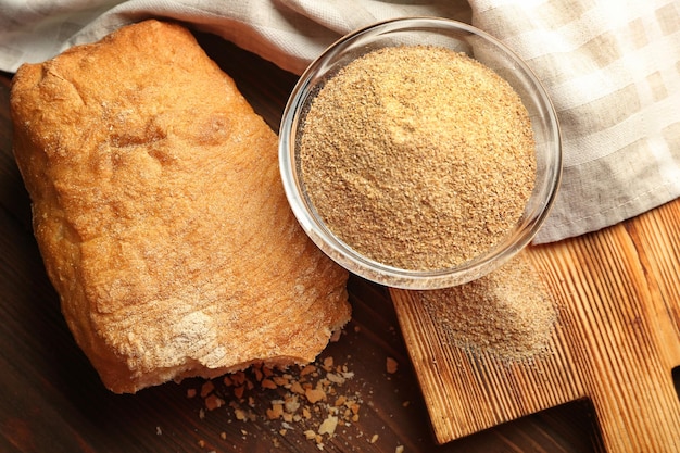 Glass bowl of bread crumbs and broken loaf on wooden table