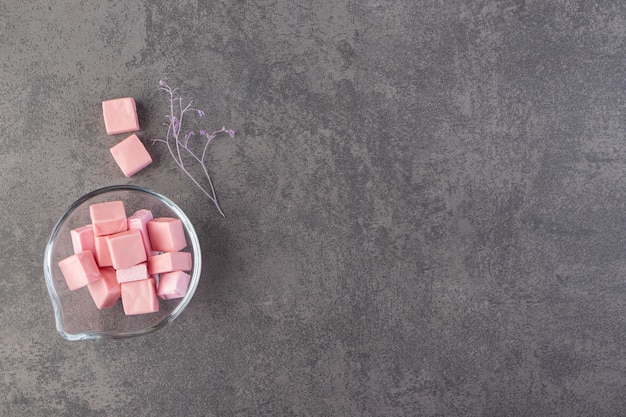 Glass bowl full of pink sliced marshmallows placed on a stone table.