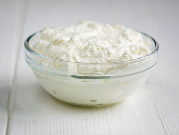 Glass bowl with cottage cheese cream on a wooden vintage white table.