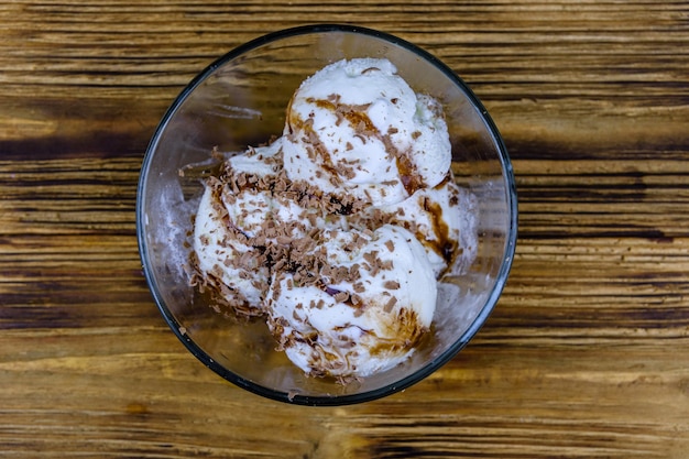 Glass bowl with ice cream balls and chocolate topping on a wooden table Top view