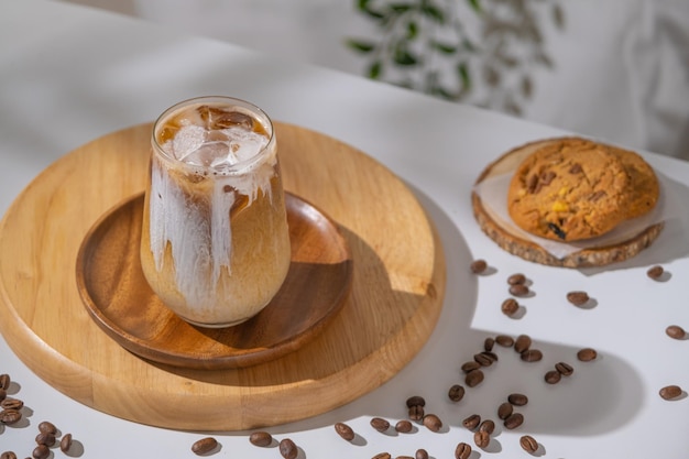 Glass of a brewing iced coffee with creamy milk and served with cookies Cold coffee drink glass with ice and cream milk on white table