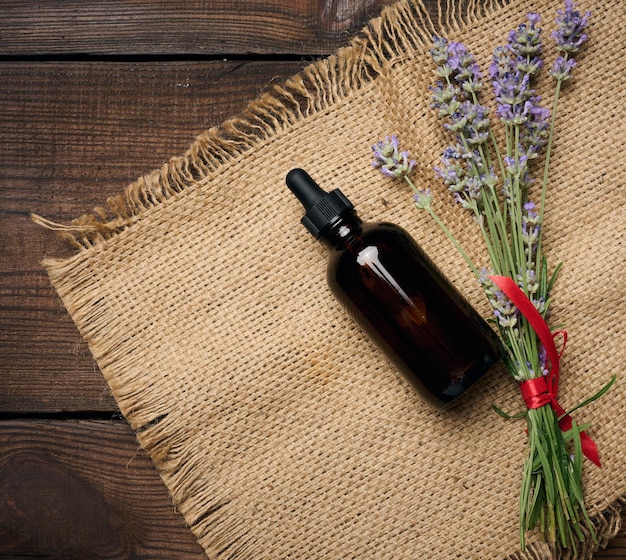 A glass brown bottle with a pipette and a bouquet of lavender on a brown wooden table