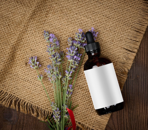 A glass brown bottle with a pipette and a bouquet of lavender on a brown wooden table