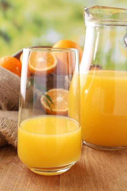 Glass and carafe of orange juice on wooden table and bright background