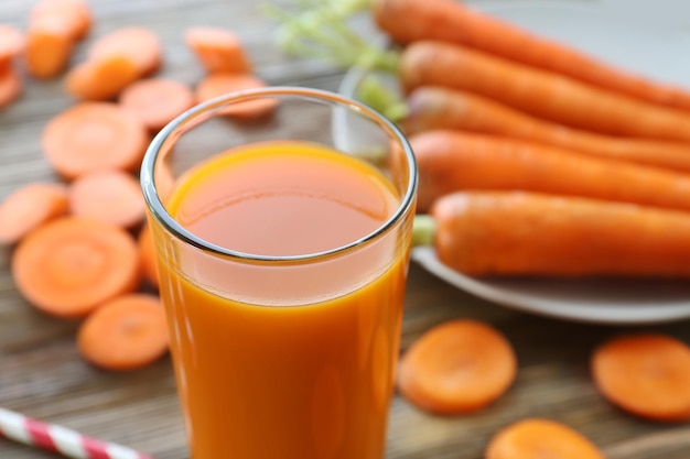 Glass of carrot juice with slices on wooden background