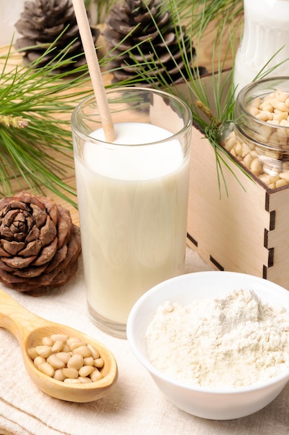 Glass of cedar milk surrounded by cones branches nuts cedar flour in white bowl Selective focus