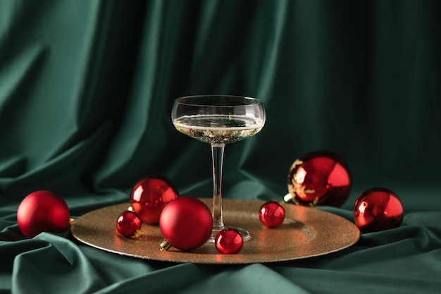 Glass of champagne with red Christmas ornaments over green velvet curtain