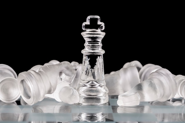 Glass chess pieces on a glass chessboard with reflection, on a black background.