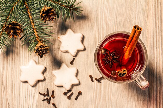 Glass of Christmas mulled wine with cinnamon, star anise and cloves on wooden background with white biscuits, natural fir tree branches and cones. Top view. Color toning effect.