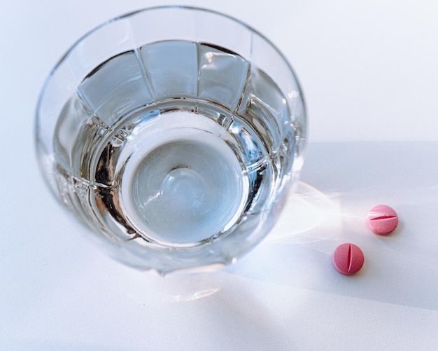 glass of clean water in rays of light and pills on table