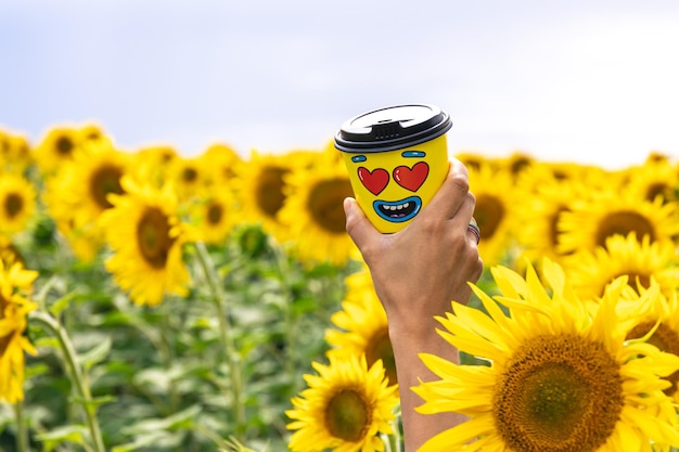 Glass of coffee in a female hand against the background of sunflowers