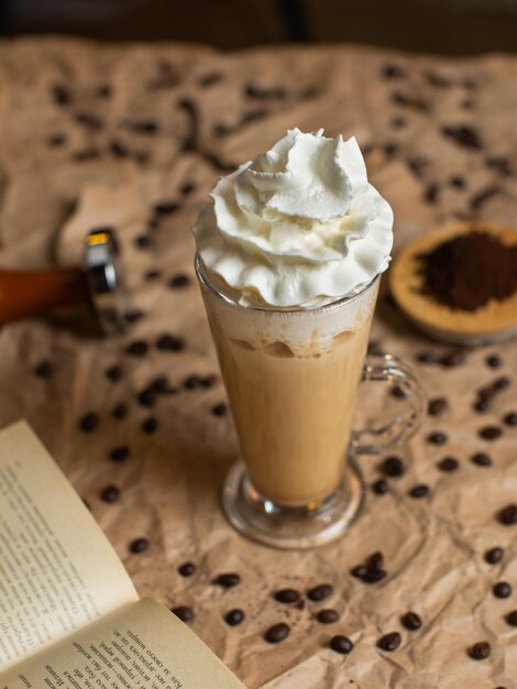 Photo a glass of coffee with whipped cream on top of it next to a book of coffee beans.