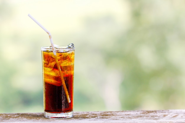 Glass of cola with ice cubes on wood table.