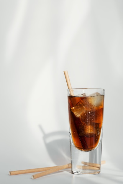 Glass of cola with ice and straw on a white wall