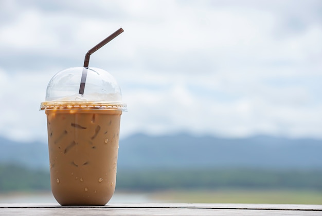 Glass of cold espresso coffee on the table Background blurry views sky water and mountain.