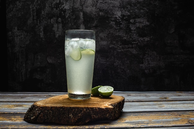 Glass of cold lemonade on wooden table. Dark background.