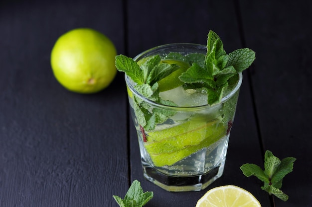 A glass of cold mojito with lime lemon and mint on a black wooden background Closeup of a refreshing cocktail