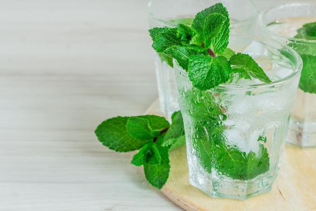 Glass of cold water with fresh mint leaves and ice cubes on wooden background