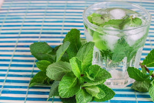 Glass of cold water with fresh mint leaves and ice cubes on wooden background