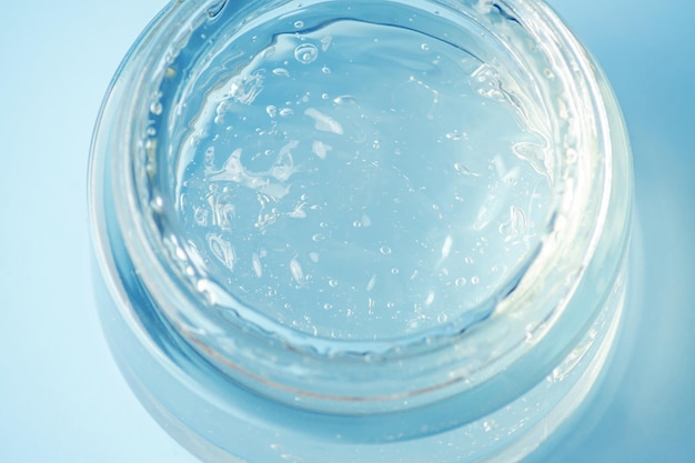 A glass container with a t moisturizing gel on a blue background. Transparent gel with bubbles.