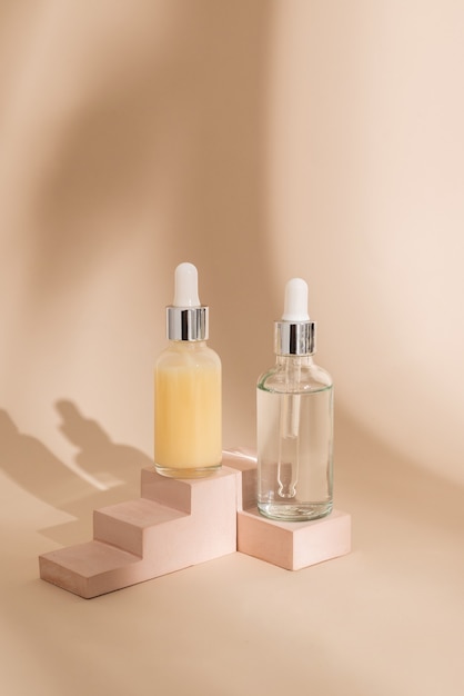 Glass cosmetic bottles with oil or serum for skin care on stone podium on beige background with hard