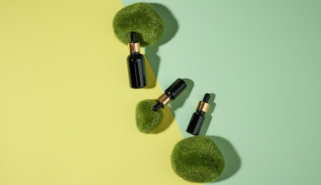 Glass cosmetic brown bottles with a pipette on a green-yellow background with pieces of moss. Cosmetics SPA branding mockup, top view