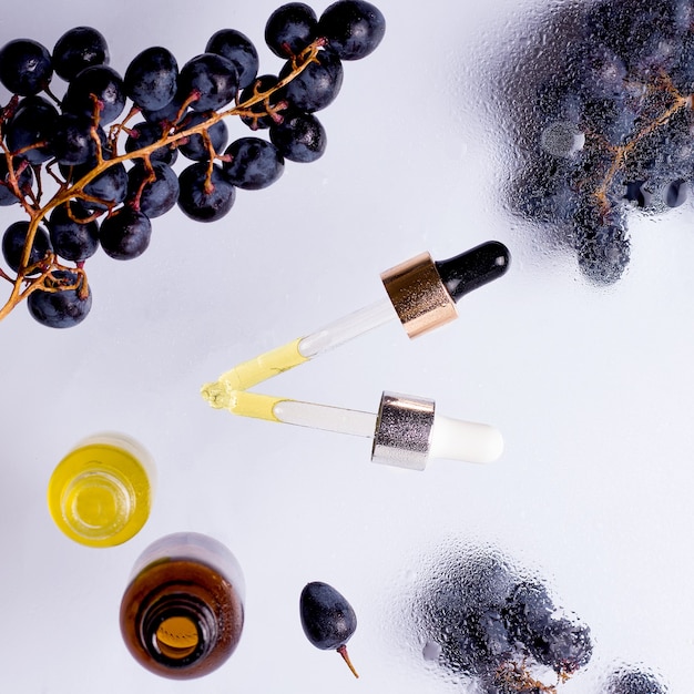 Glass cosmetic oils pipettes and bottles  with  black grapes around on wet trasnlucid background