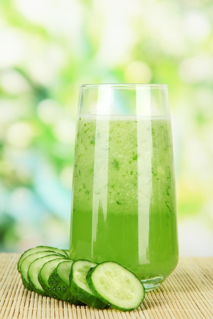 Glass of cucumber juice on bamboo mat on green background