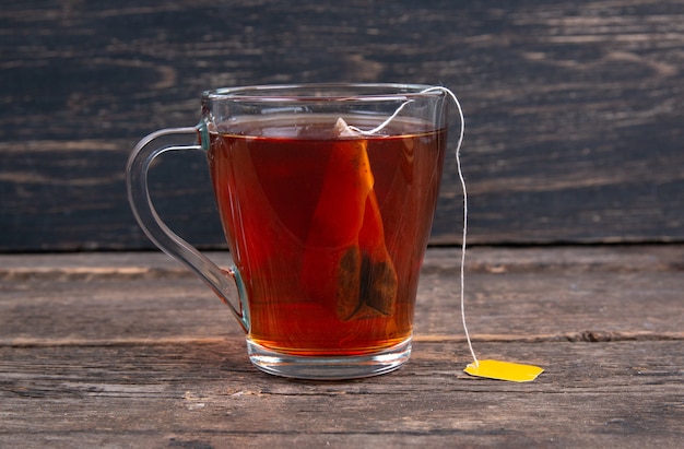 Glass cup of black tea with tea bag on a wooden table